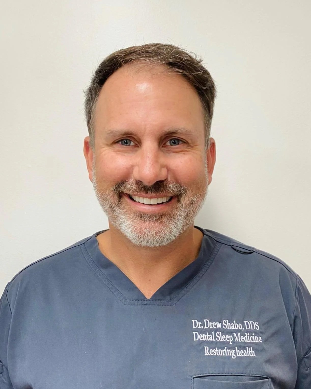 Dr. Drew Shabo, DDS, wearing blue scrubs